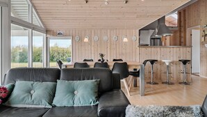 Een modern interieur met een houten plafond, een zwarte leren bank, een eettafel met stoelen en een barhoek.