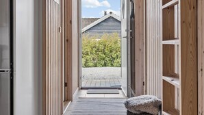 Een houten binnenhal die leidt naar een deur, met uitzicht op een huis en bomen.