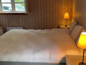 Une chambre à coucher avec un grand lit, des murs en bois, une fenêtre et une lampe de chevet.