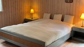 Um quarto com parede revestida de madeira, uma cama com roupa de cama branca, duas mesas de cabeceira com abajures e um relógio na parede.