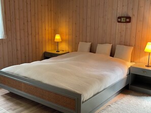 Ein Schlafzimmer mit einer holzverkleideten Wand, einem Bett mit weißer Bettwäsche, zwei Nachttischen mit Lampen und einer Wanduhr.