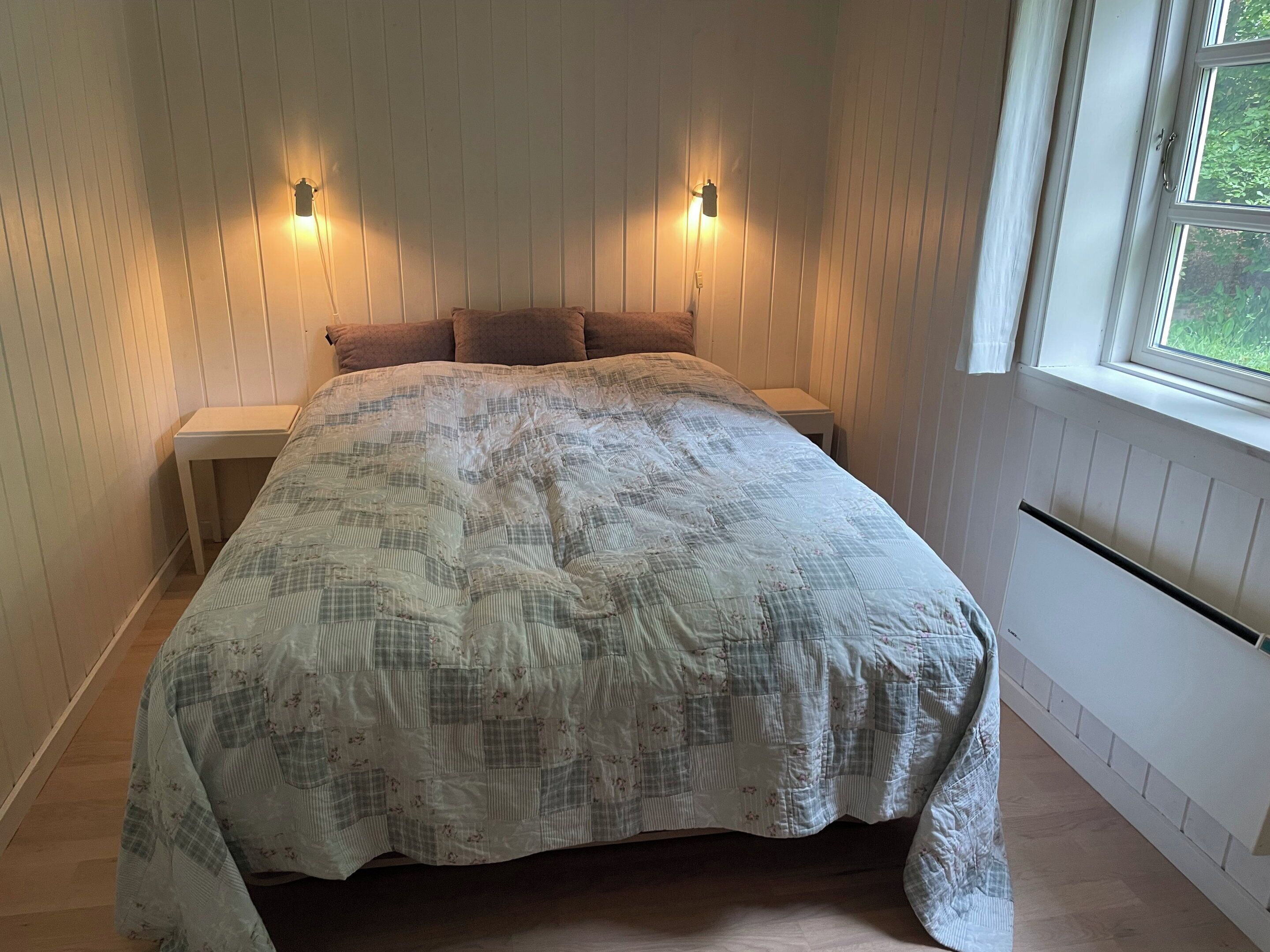 Un dormitorio con una cama grande, dos mesitas de noche, una ventana y luces fijadas a la pared.