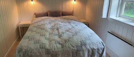 Un dormitorio con una cama grande, dos mesitas de noche, una ventana y luces fijadas a la pared.
