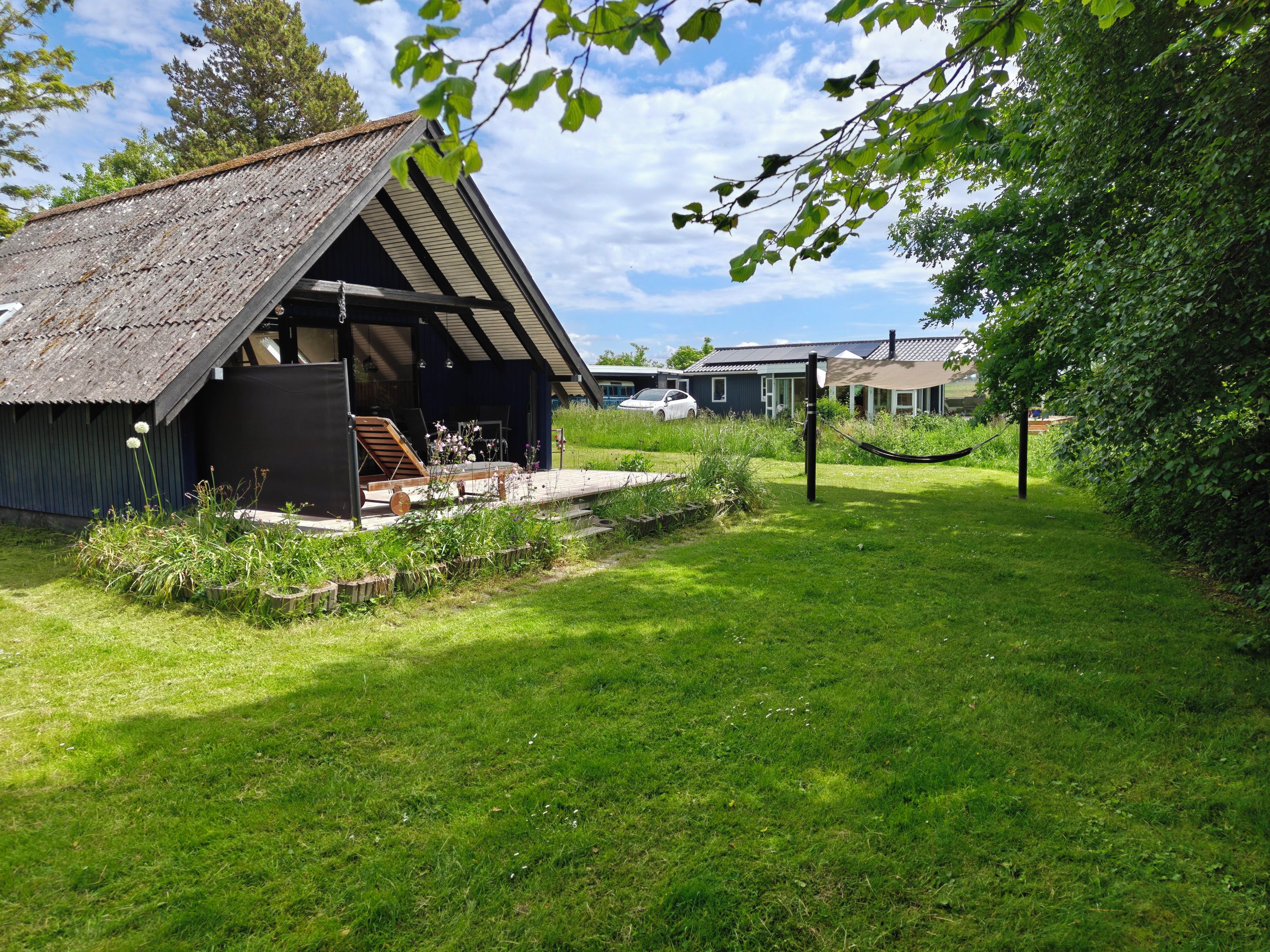 A rustic building with a sloped roof, a wooden deck, and a garden area with grass and plants.