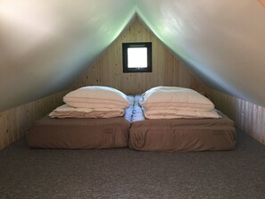 Ein kleines, dreieckiges Schlafzimmer im Dachgeschoss mit einem Fenster, zwei Betten mit Kissen und Teppichboden.