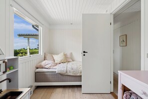 A room with a bed, a window, a door, and a small kitchen area. - Cozy family holiday home with beautiful view (Fårevejle)
