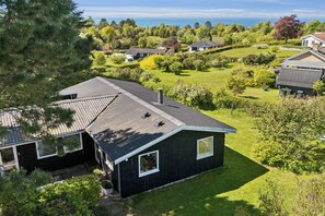 A residential area with houses, a well-maintained lawn, and a large tree. - Cozy family holiday home with beautiful view (Fårevejle)