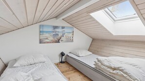 Een slaapkamer met een schuine plafond, een dakraam, twee bedden, een nachtkastje en een aan de muur hangend schilderij.