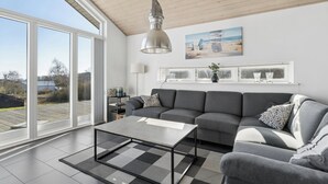 Een moderne woonkamer met een grijze bank, een salontafel en een groot raam met uitzicht op de omgeving.