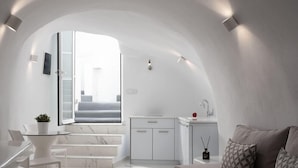 A modern, minimalist interior with a white color scheme, featuring a kitchen, dining area, and a cozy seating space with a sofa and cushions. - White Concept Caves - Adults Only (Santorini)