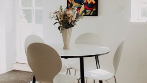 A dining area with a white table, four chairs, a vase with flowers, and a colorful abstract painting on the wall.