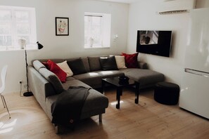 Ein modernes Wohnzimmer mit einem grauen Ecksofa, einem kleinen schwarzen Tisch und einem weißen Kühlschrank.