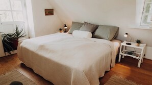 A bedroom with a large bed, two bedside tables with lamps, a potted plant, and a window with a view.