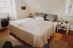 Ein Schlafzimmer mit einem großen Bett, zwei Nachttischen mit Lampen, einer Topfpflanze und einem Fenster mit Blick.