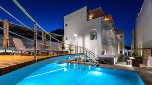 Una piscina interior con una terraza de madera, sillas de descanso y una escalera que lleva a un nivel superior.