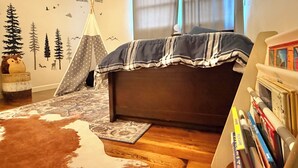Een slaapkamer met een bed, een boekenkast, een vloerkleed, een vachtkleed, een tentdecoratie en behangstickers.