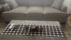 Een woonkamer met een bank, een bijzettafeltje met geruit tafelkleed en een lamp.