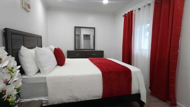 Un dormitorio con cama, cómoda, espejo y cortinas rojas.