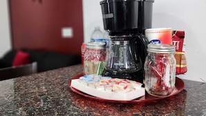 Una encimera de cocina con una cafetera, frascos de especias y un plato con vasos de yogur.