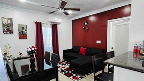 Una sala de estar moderna con un sofá negro, una mesa de comedor con sillas, una zona de cocina con mostrador y un ventilador de techo.