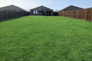 A backyard with a wooden fence, a covered patio, and a house in the background.