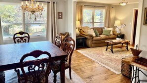 A dining area with a wooden table and chairs, a chandelier, and a view of the outdoors through large windows. - Panther Creek Cozy Retreat (Newton)