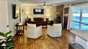 A living room with a brown sofa, two white armchairs, a wooden floor, and a ceiling fan. - Panther Creek Cozy Retreat (Newton)