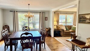 A dining area with a wooden table and chairs, a chandelier, and a view of the outdoors through large windows. - Panther Creek Cozy Retreat (Newton)