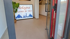 A hotel lobby with a reception desk, a framed cityscape artwork, and a glass door leading to another room. - Bologna Rooms & Art (Bologna)