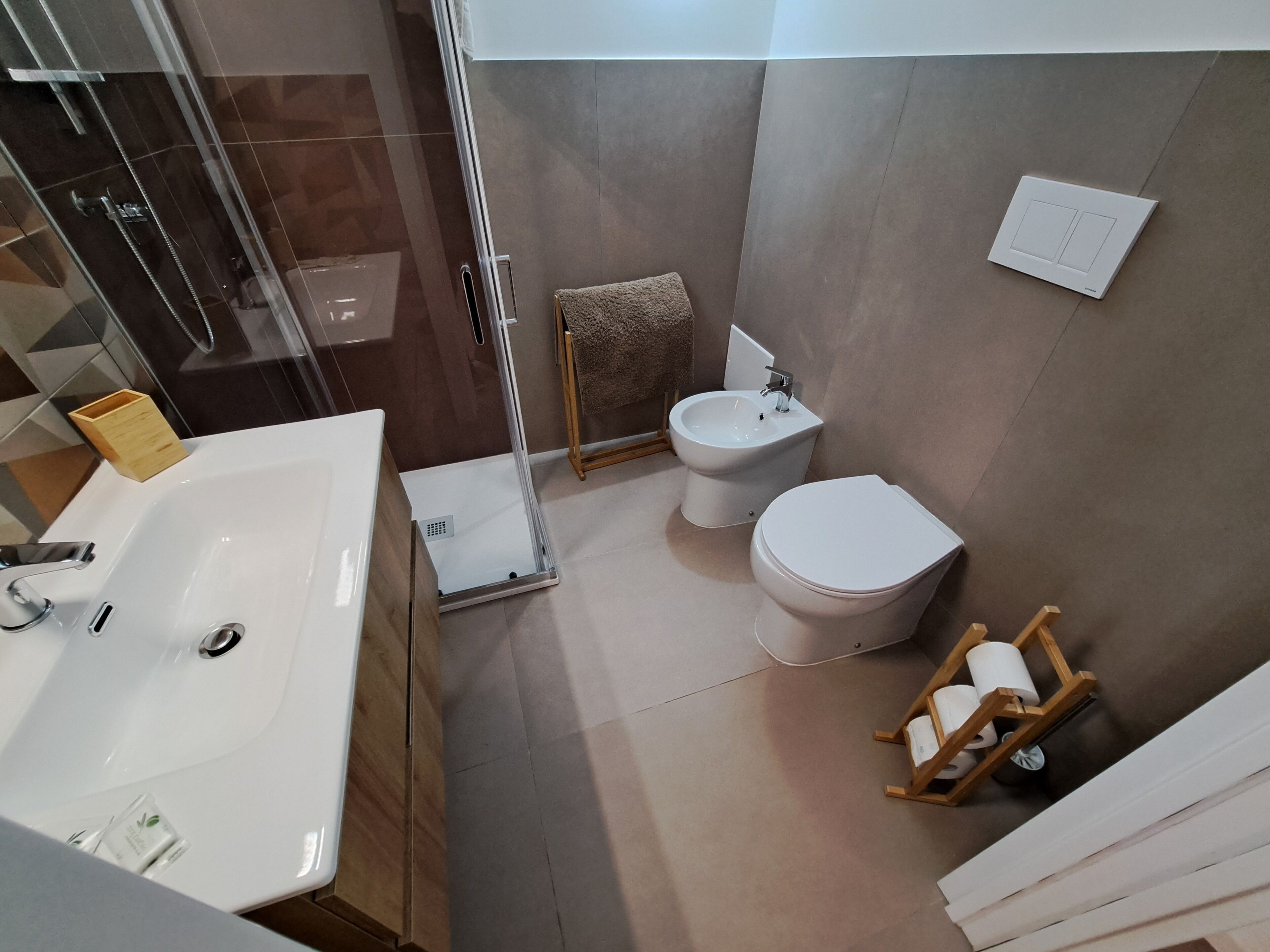 Un baño moderno con ducha de vidrio, lavamanos blanco, un bidé y un inodoro.