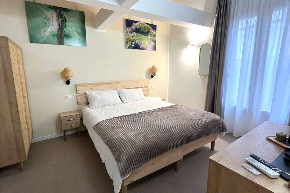 Ein Schlafzimmer mit einem Bett, Nachttischen, einem Schreibtisch mit Stuhl, einem Spiegel und Bildern an den Wänden.
