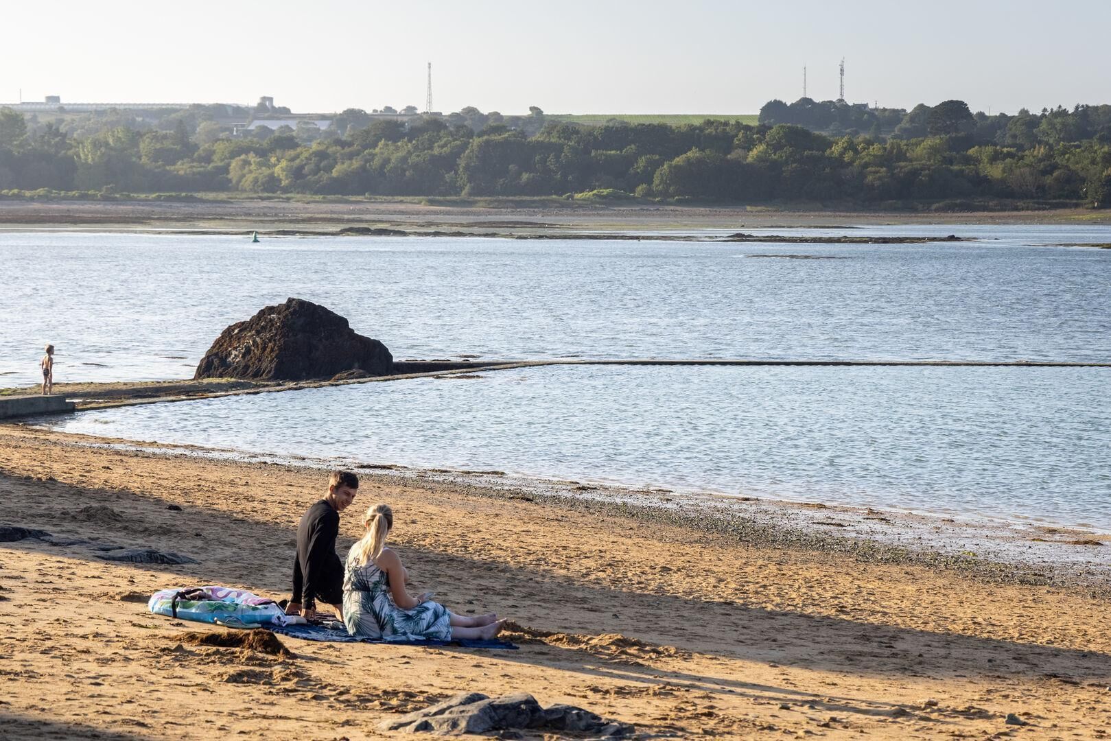 A beach with a rocky outcrop and calm water.