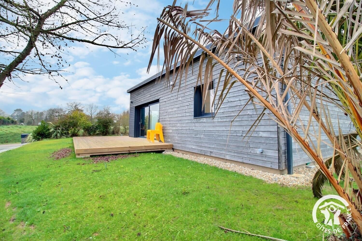 A modern house with a wooden exterior, a deck, and a yellow chair.