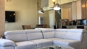 A modern living room with a sectional sofa, a glass coffee table, and pendant lighting.