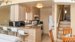 A modern kitchen with a central island, bar stools, and a dining area with wooden chairs.