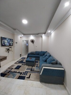 A living room with a sectional sofa, a flat-screen TV mounted on the wall, and a patterned rug. - COZY CLUB STUDIO (Giza Governorate)