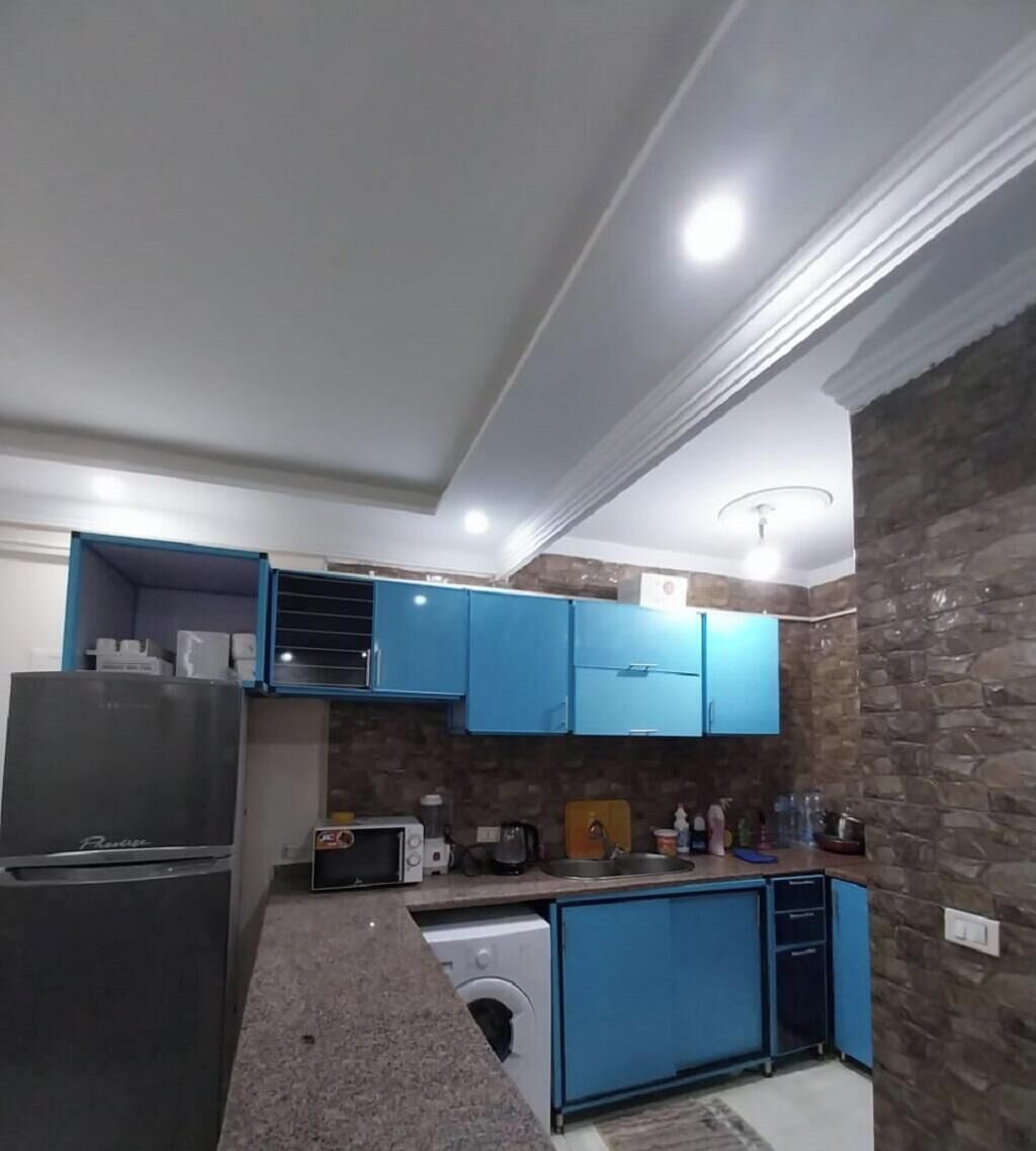 Una cuina compacta amb armaris blaus, rentadora integrada i nevera.
