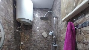 Un bagno con parete in pietra, un water, un lavandino, una doccia con soffione a pioggia e un asciugamano su un porta asciugamani.