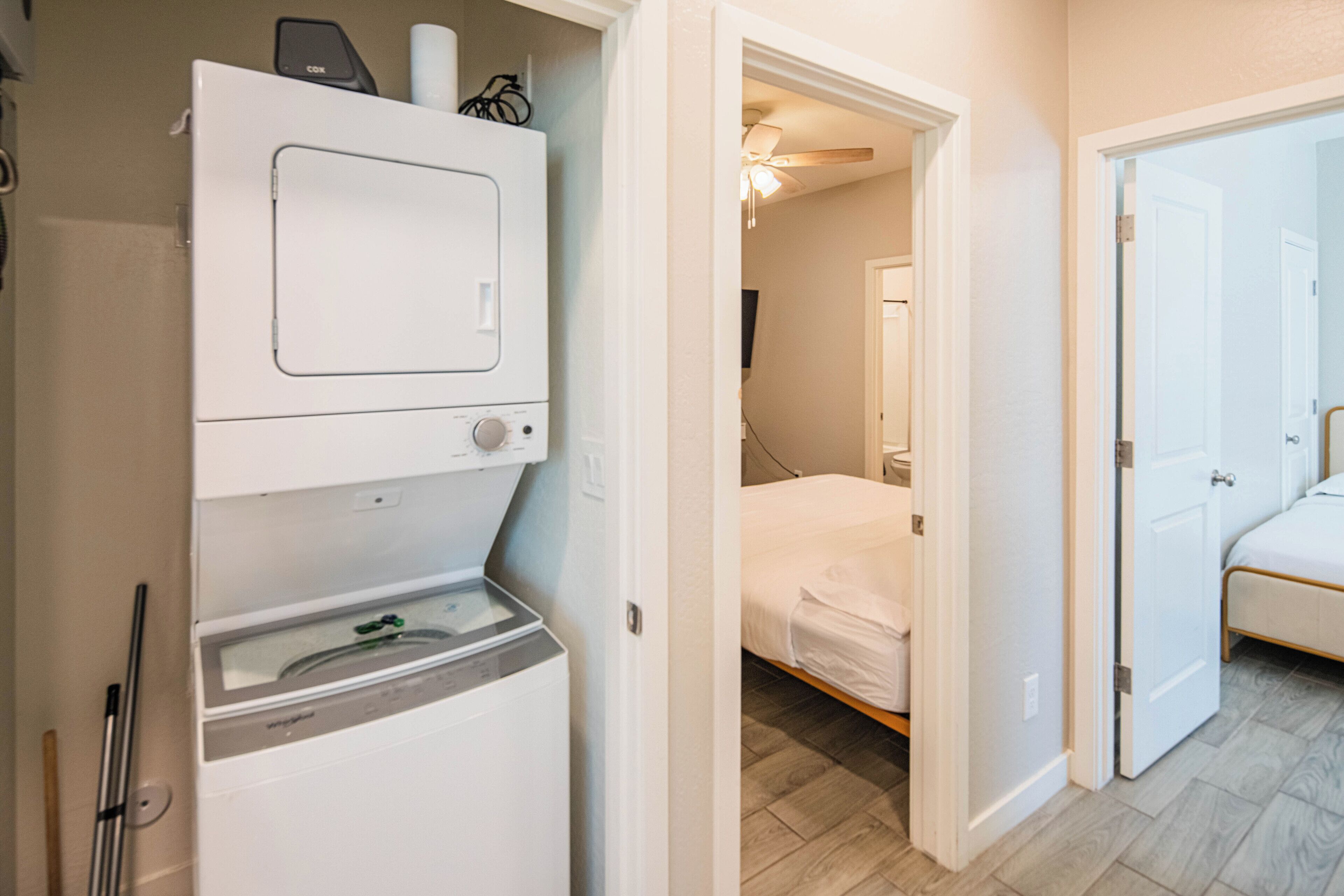 A laundry room with a washer and dryer, a hallway leading to a bedroom with a bed and a ceiling fan.