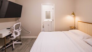 Una camera d'albergo con un letto, una scrivania con una sedia, una televisione, una lampada da comodino e un ingresso che dà su un bagno.