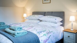 Siististi pedattu sänky, jossa on kukallinen vuodevaatesetti, kaksi yöpöytävalaisinta ja pieni yöpöytä, jossa on myös valaisin.