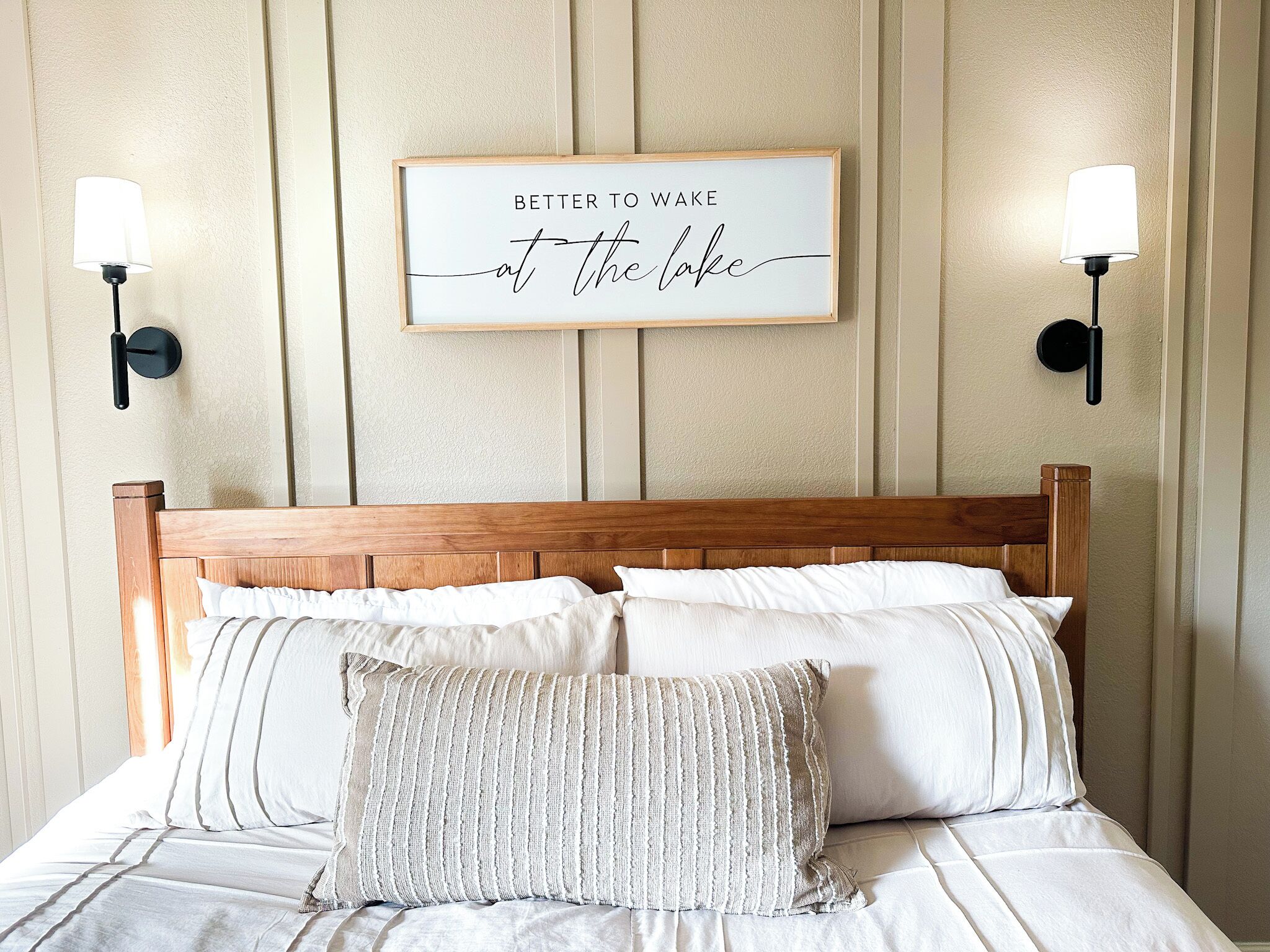 A neatly made bed with a wooden headboard, two wall-mounted lamps, and a framed motivational quote on the wall.
