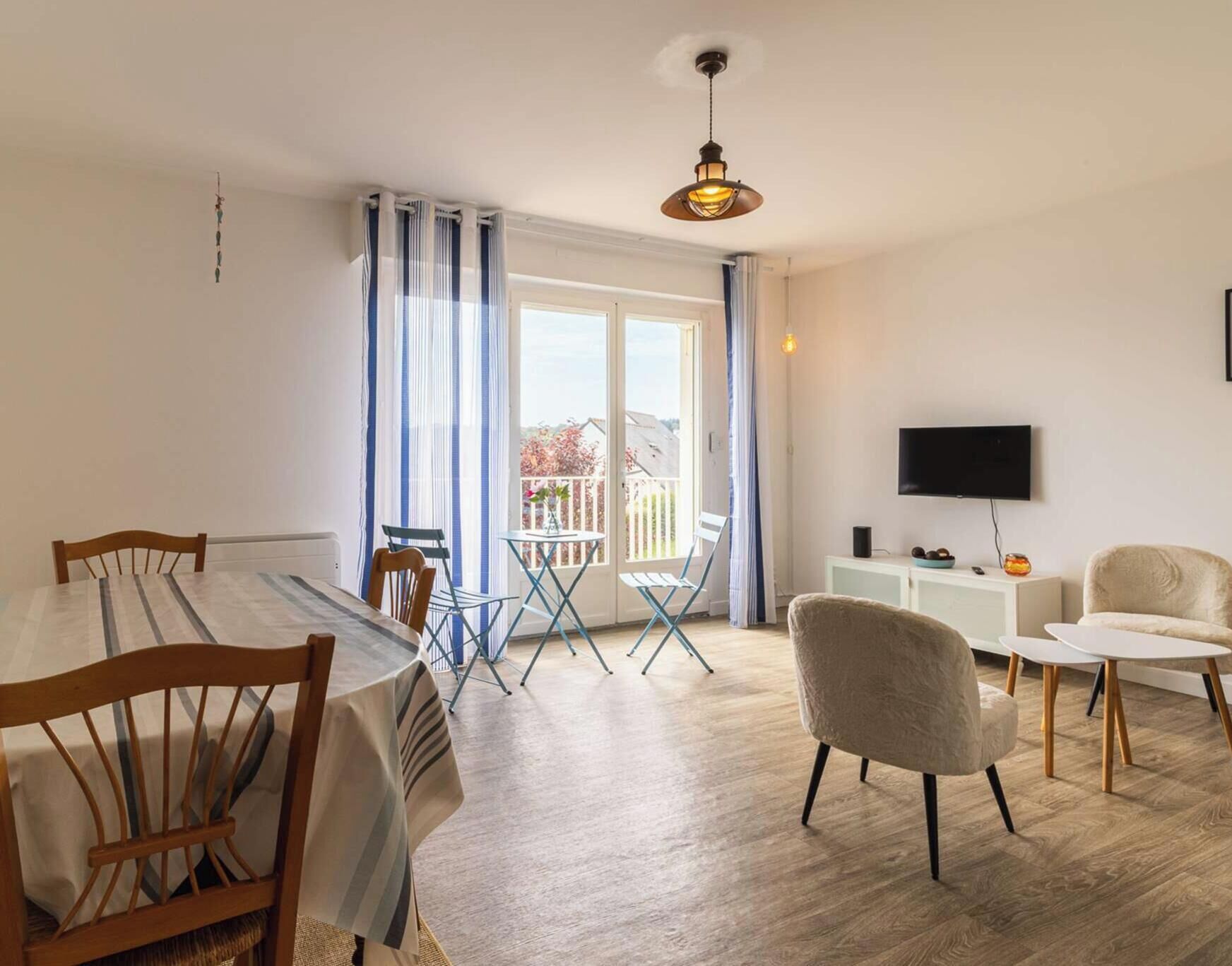 A modern room with a dining table, chairs, a sofa, a TV, and a balcony with curtains.