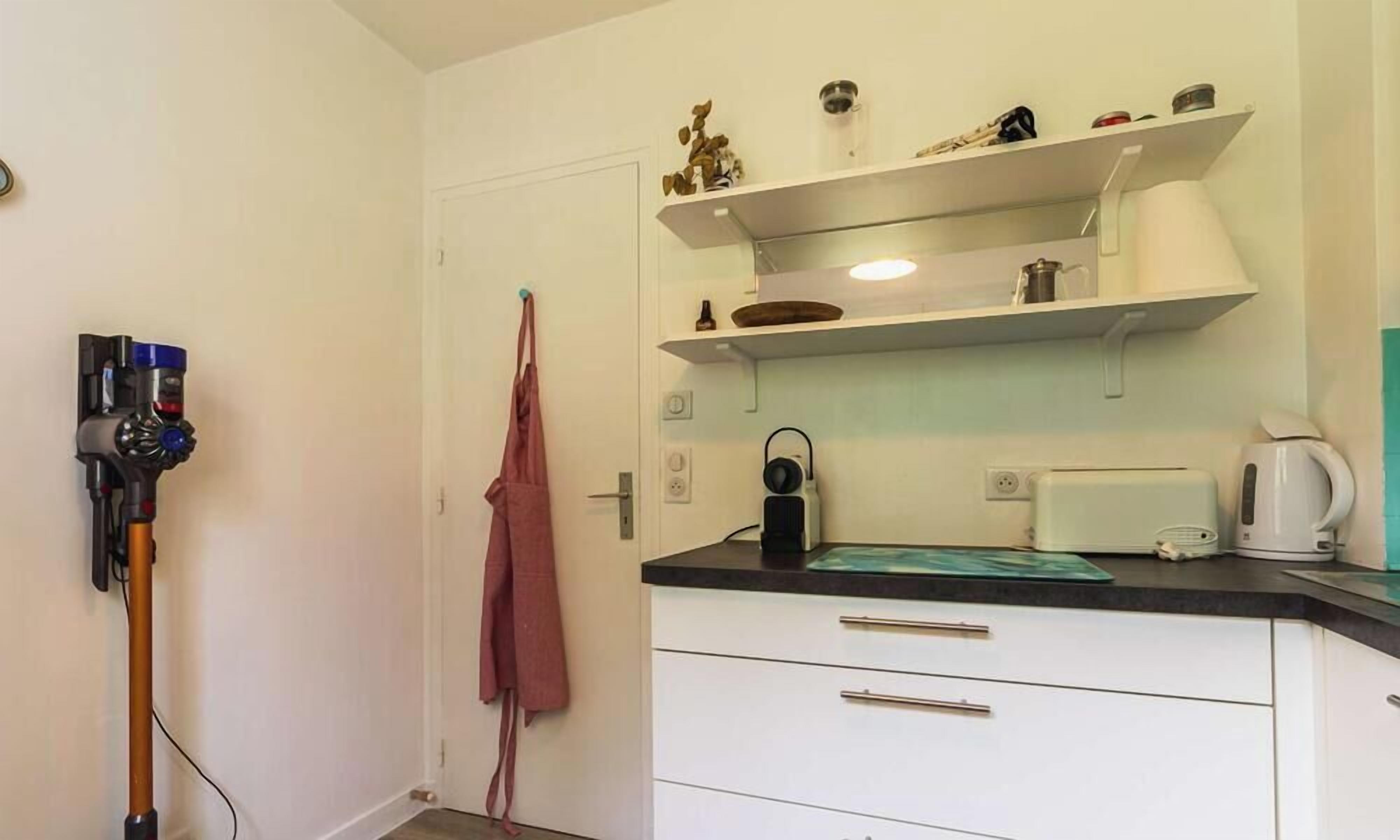 Een kleine keuken met witte kasten, een zwart aanrecht, een waterkoker en een koffiezetapparaat.
