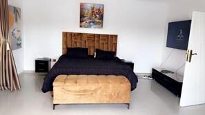 A modern bedroom with a large bed, a wooden headboard, a TV, and a painting on the wall. - Holiday Villa Marondera (Marondera)