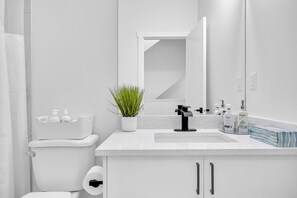 Moderni kylpyhuone, jossa on valkoinen wc-istuin, mustalla hanalla varustettu pesuallas, peili ja hygieniatuotteita tasolla.