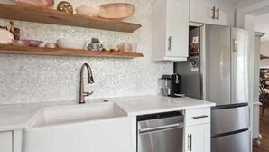 A modern kitchen with white cabinetry, stainless steel appliances, and decorative items on shelves.