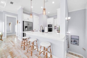 A modern kitchen with white cabinetry, a central island with stools, and pendant lighting. - Vacay on 30A by Stay on 30a (Inlet Beach)