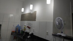 Un baño con azulejos blancos, un perchero, un ventilador y un dispensador de agua.