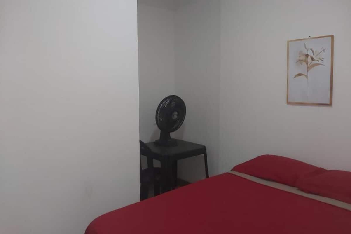 Una habitación con cama, escritorio y ventilador.